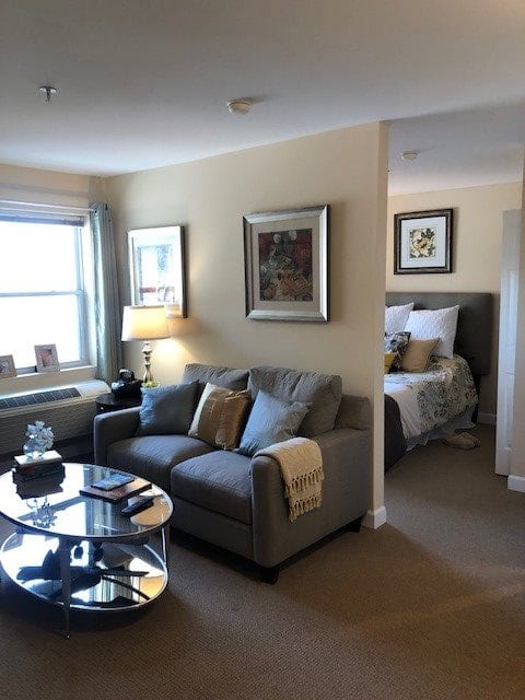 A cozy living room with a view into the bedroom, featuring a comfortable sofa, lamp, and decorative artwork.