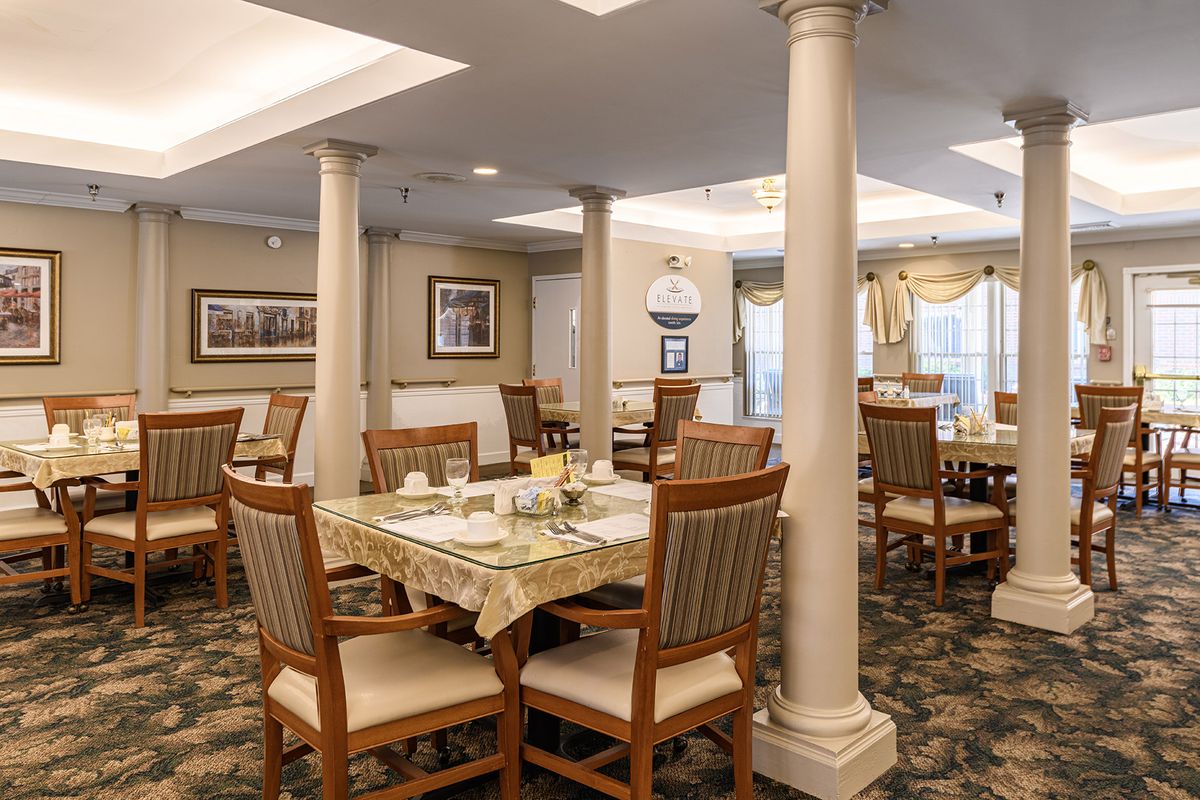 A cozy dining room with neatly set tables and comfortable seating, featuring elegant columns and tasteful decor.