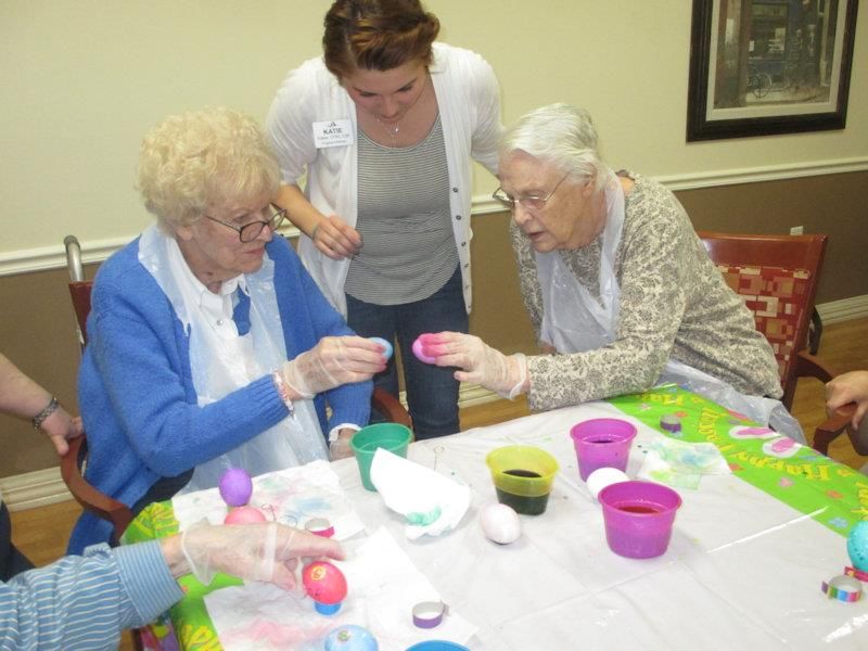 Elderly women engage in a fun egg dyeing activity, assisted by a caregiver.