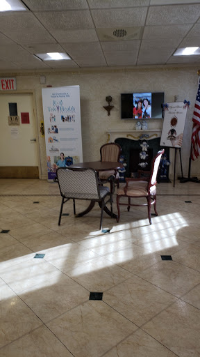 A cozy lobby area featuring a table and chairs, with a television displaying images, banners on display, and natural light illuminating the space.