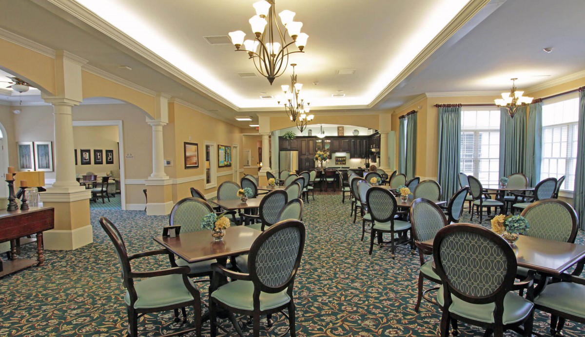 An elegant dining room with multiple tables and chairs, illuminated by chandeliers.