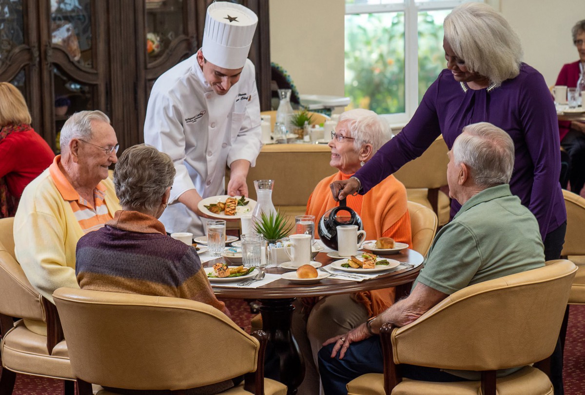 A chef serves food to a group of seniors dining together.