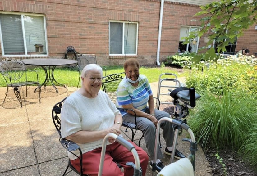 Two elderly individuals sitting outside with walkers, enjoying a sunny day.