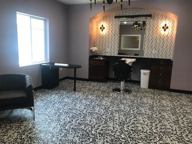 A chic salon interior with stylish lighting, patterned carpet, and a large mirror.