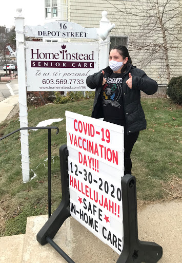 A woman stands by a sign promoting a COVID-19 vaccination day, expressing excitement about the event.