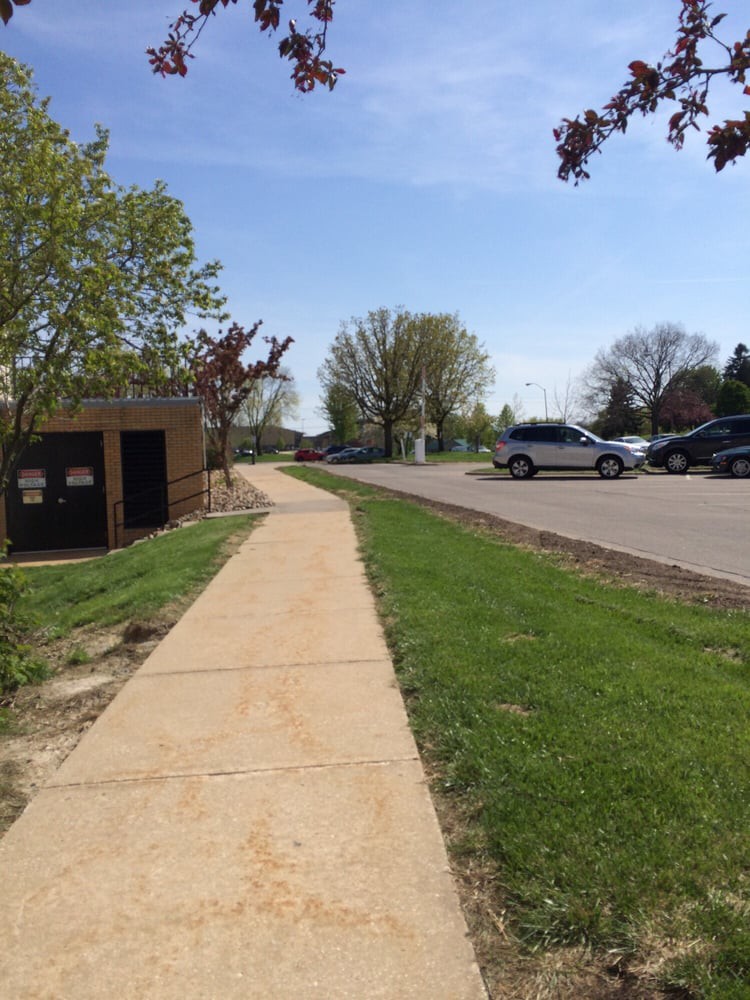 A sidewalk next to a parking lot with cars and trees on a sunny day.