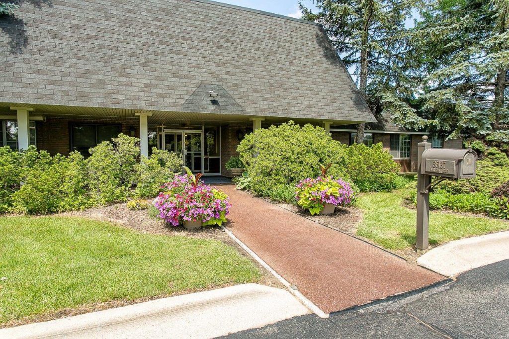 A garden pathway leads to the entrance of a building, surrounded by lush greenery and colorful flowers.