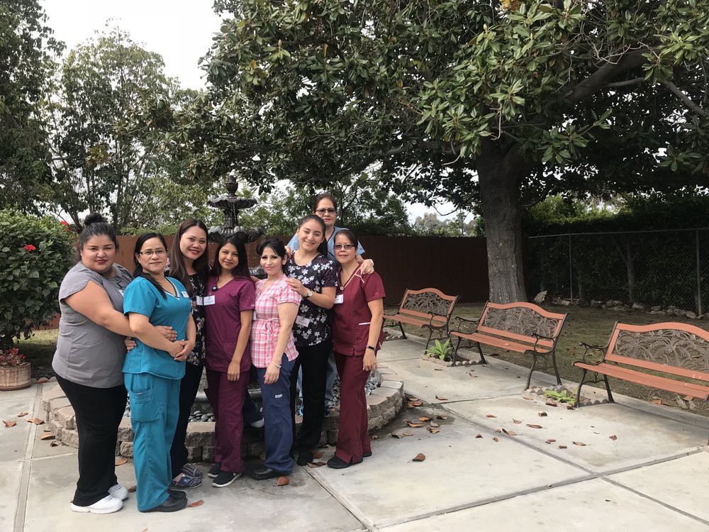 A group of people standing together in a garden setting with benches and trees in the background.