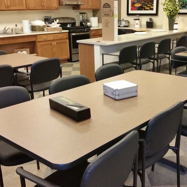 A well-equipped office break room with tables and chairs, featuring a kitchen area with appliances.