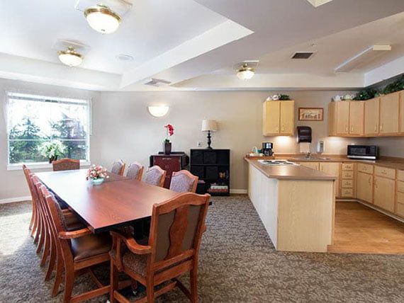 A spacious dining and kitchen area with a large wooden table, chairs, and bright ceiling lights.