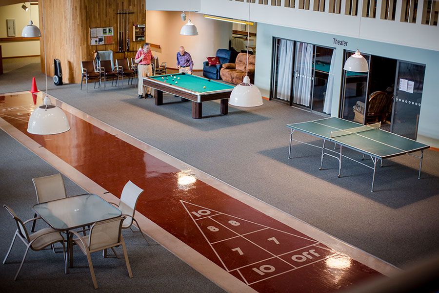 A spacious indoor game room featuring a billiards table, shuffleboard court, and table tennis setup.