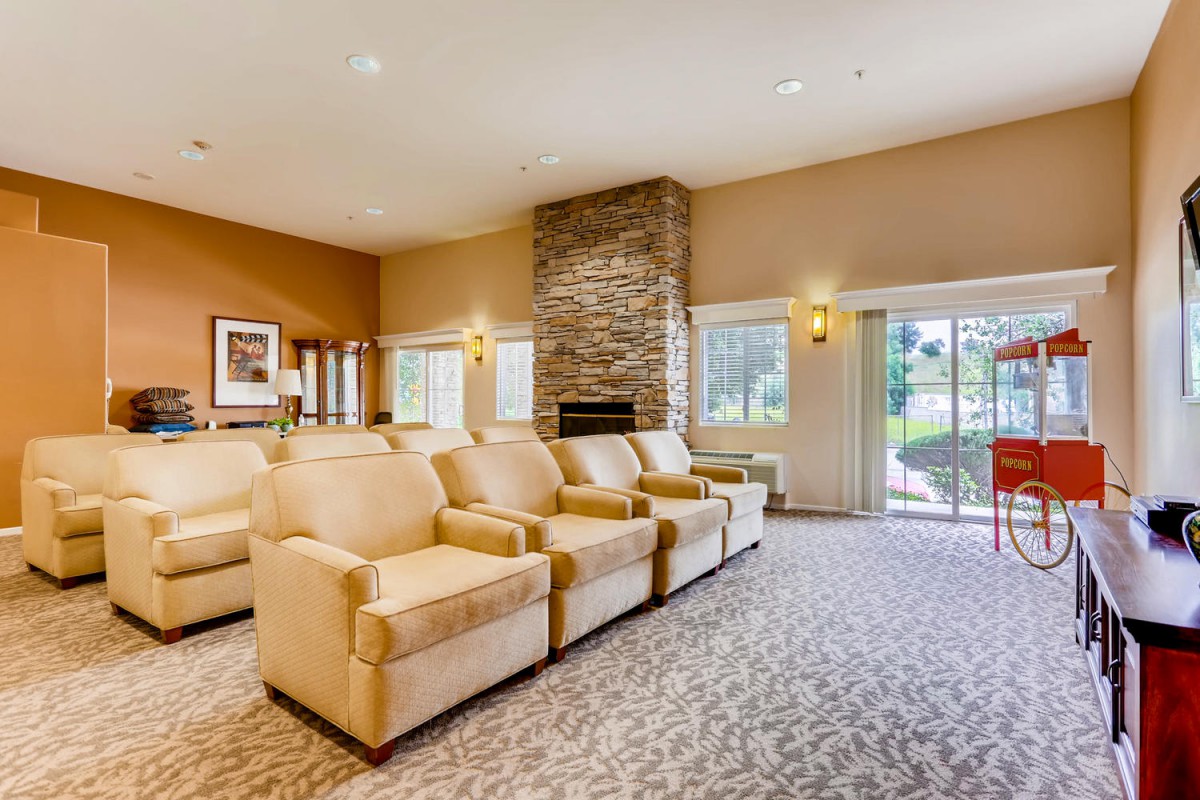 A cozy living room with a row of comfortable armchairs facing a stone fireplace, complemented by large windows and warm lighting.