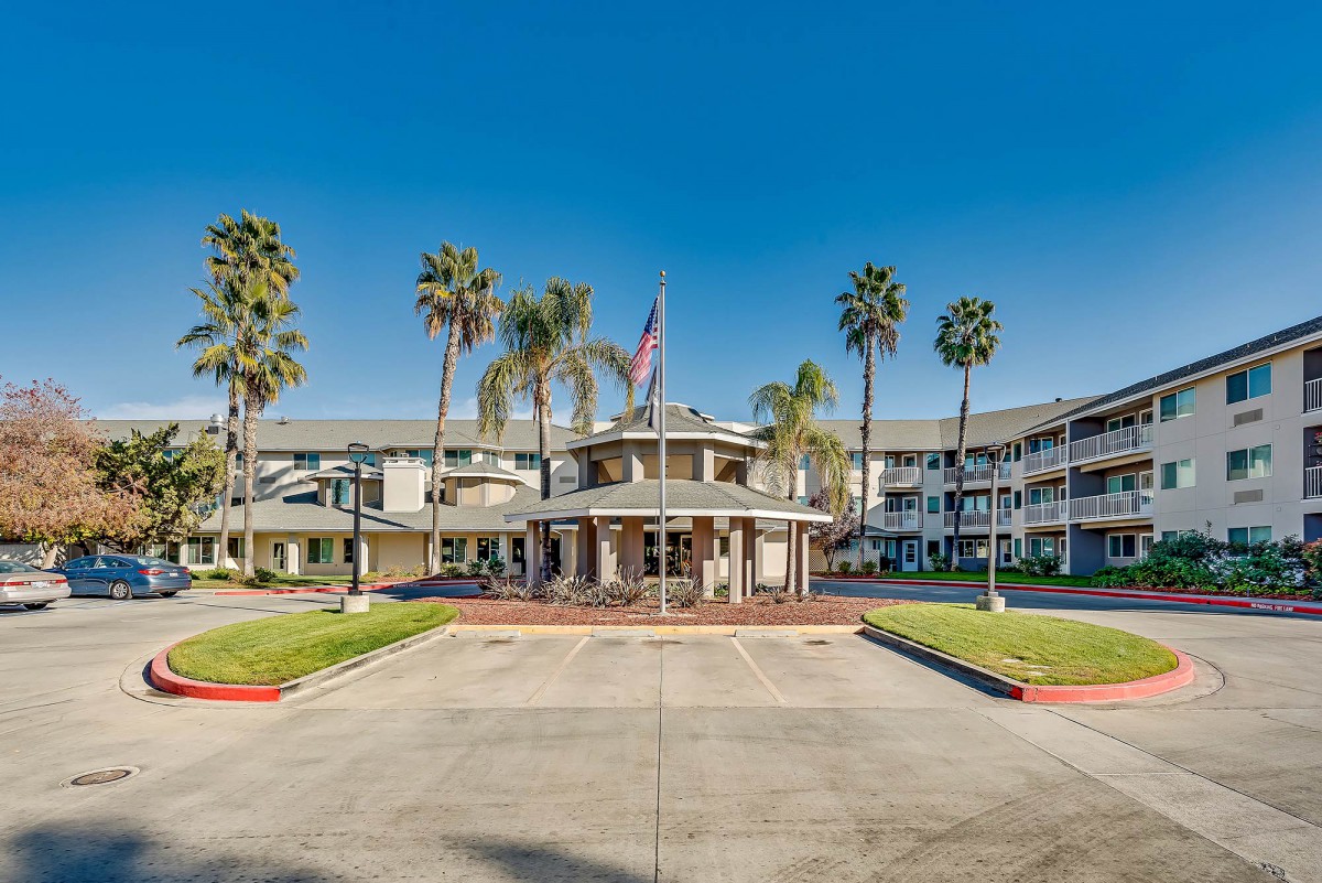 A hotel building with palm trees and an entrance driveway, featuring a flag at the entrance.