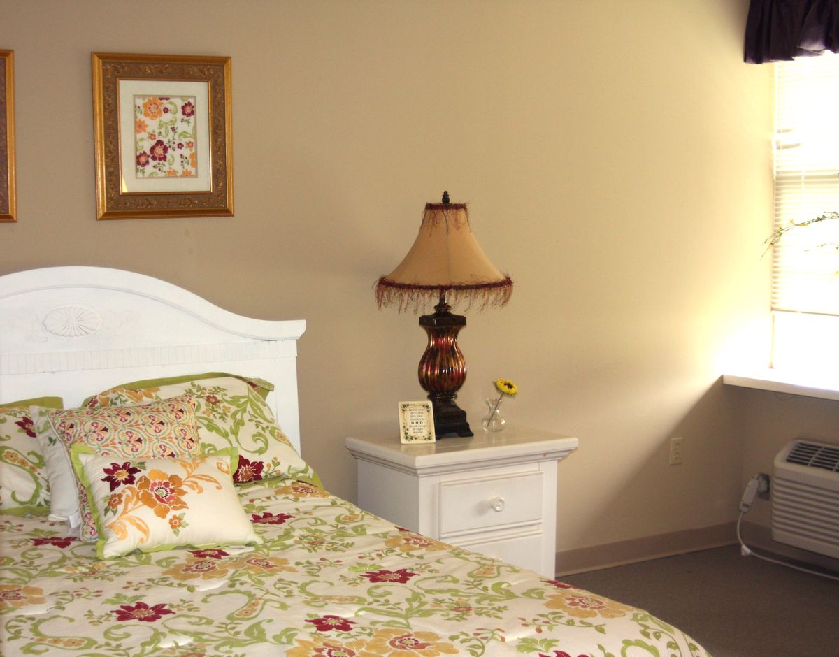 A cozy bedroom with a floral bedspread, nightstand, and decorative lamp.