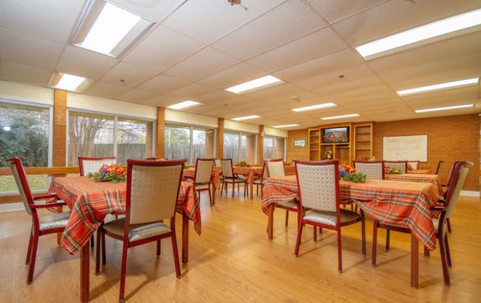 A spacious dining room with neatly arranged tables and chairs, featuring warm lighting and wood flooring.