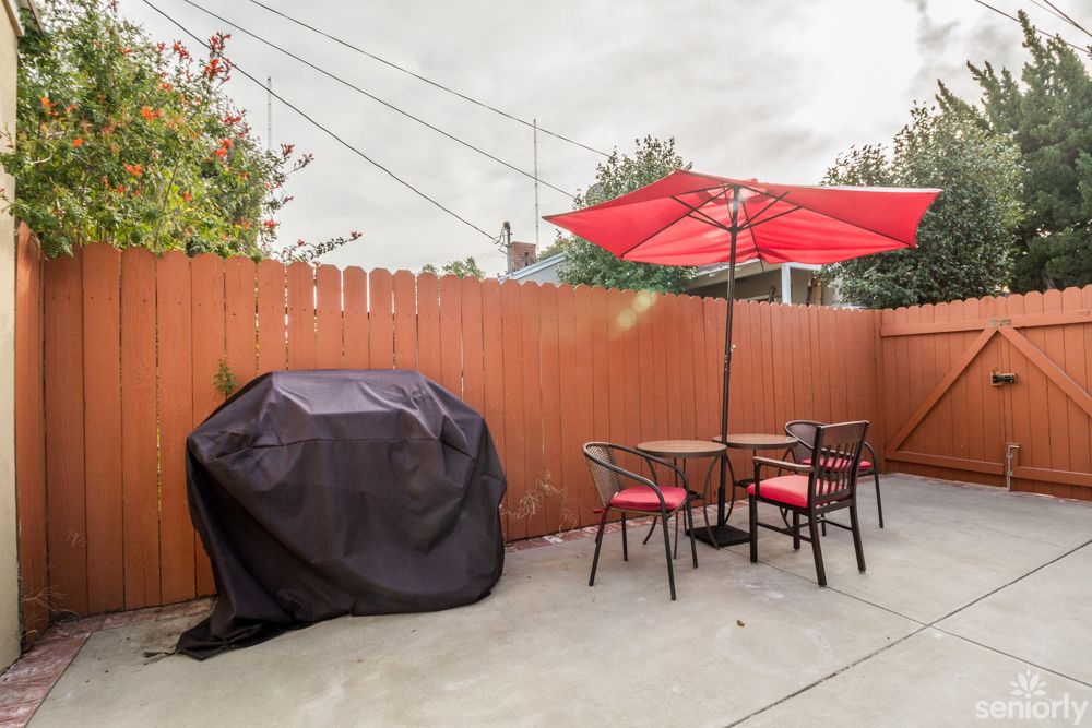 A cozy patio with a table and chairs under a red umbrella, next to a covered grill.