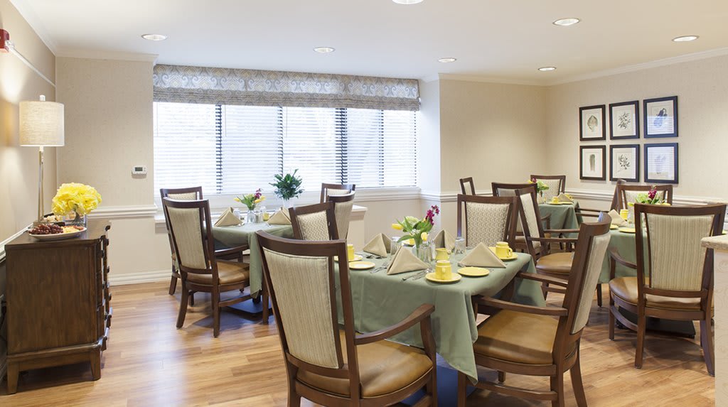 A well-lit dining room with neatly arranged tables and chairs, adorned with flowers and set for a meal.