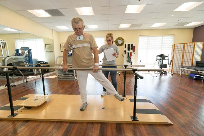 A senior individual undergoing physical therapy with the assistance of a therapist in a healthcare facility.