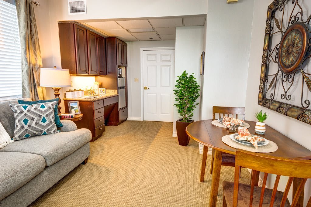 A cozy living space featuring a sofa, dining table set for two, and a small kitchenette with dark cabinets.