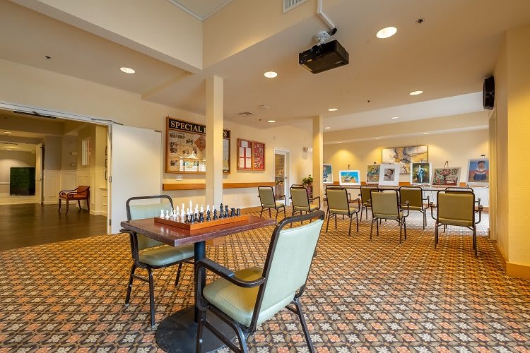 A well-lit room with a chessboard on a table, surrounded by chairs, and decorated with artwork.