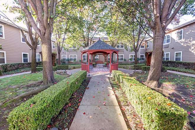 A peaceful garden pathway leading to a red gazebo surrounded by lush greenery in a residential area.