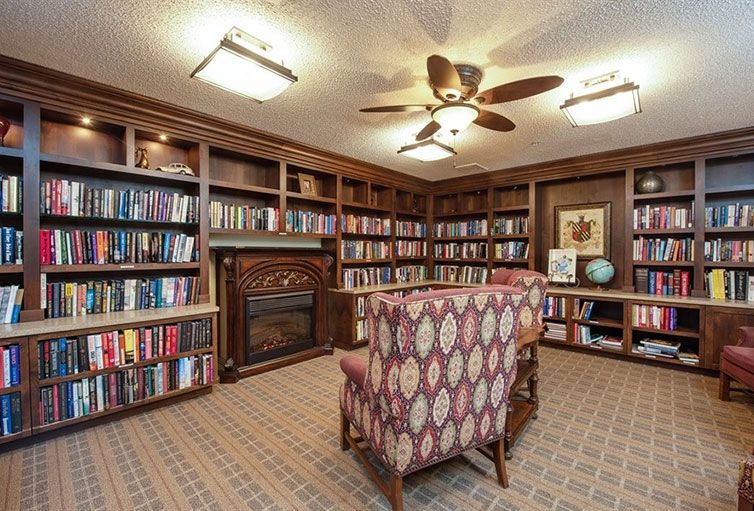 A cozy library with rows of bookshelves, armchairs, and a warm fireplace.