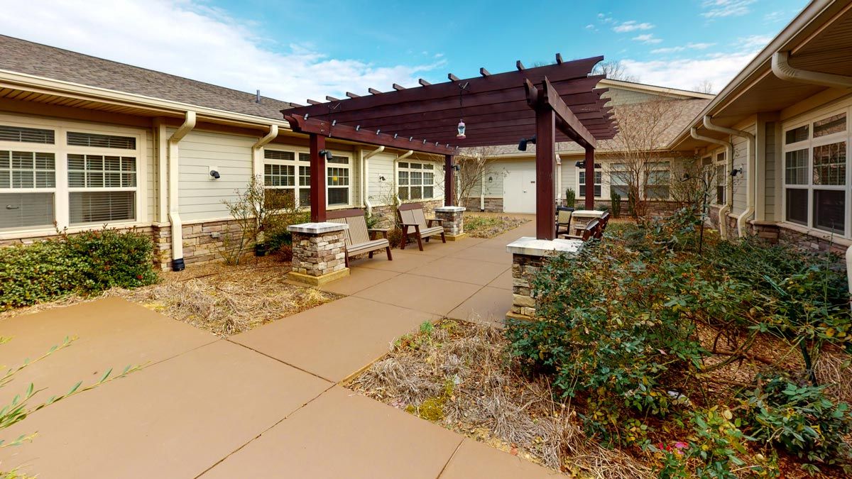 An inviting patio with a pergola and benches, surrounded by landscaping and a paved pathway.