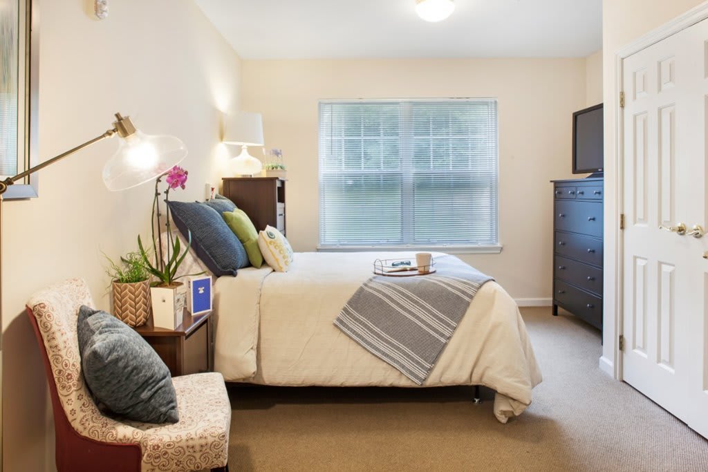 A cozy bedroom with a neatly made bed, colorful cushions, and a large window letting in natural light.