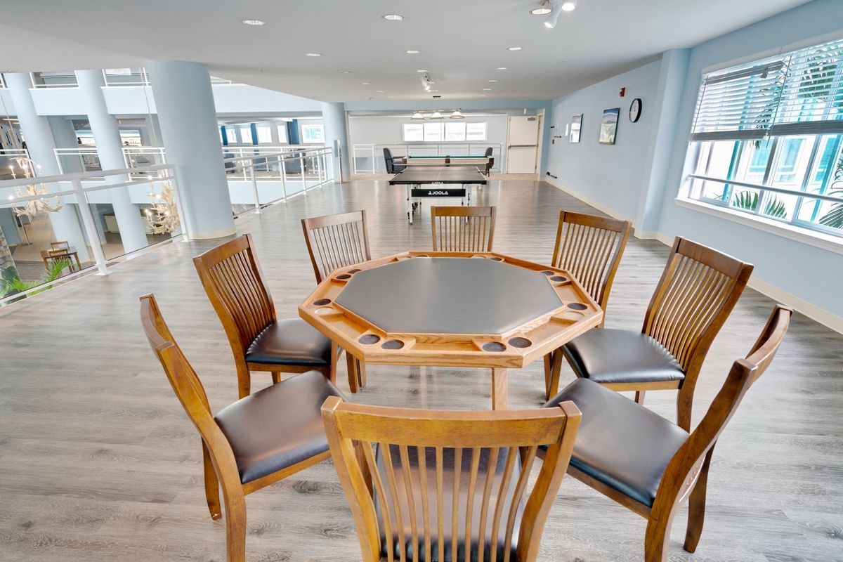 A modern and spacious game room featuring a central poker table surrounded by wooden chairs.