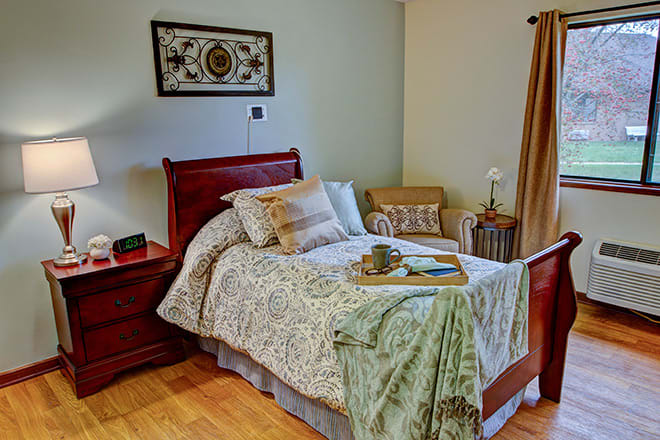 A cozy bedroom with a neatly made bed, a side table, and an armchair in the corner.