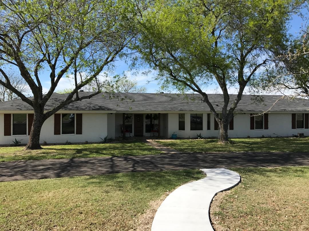 A single-story house with a curved pathway leading to the entrance, surrounded by trees in the front yard.