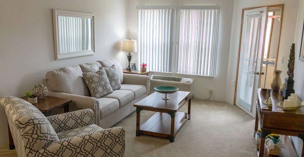 A cozy living room with a sofa, armchair, and coffee table near a window with blinds.