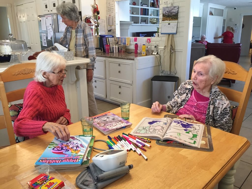 Two seniors engaged in coloring activities at a kitchen table.