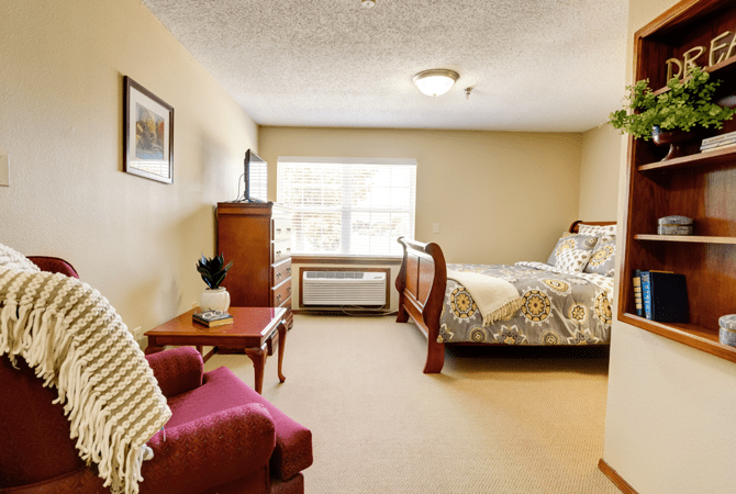 A cozy, well-furnished bedroom with a large bed, armchair, and natural light streaming in through the window.