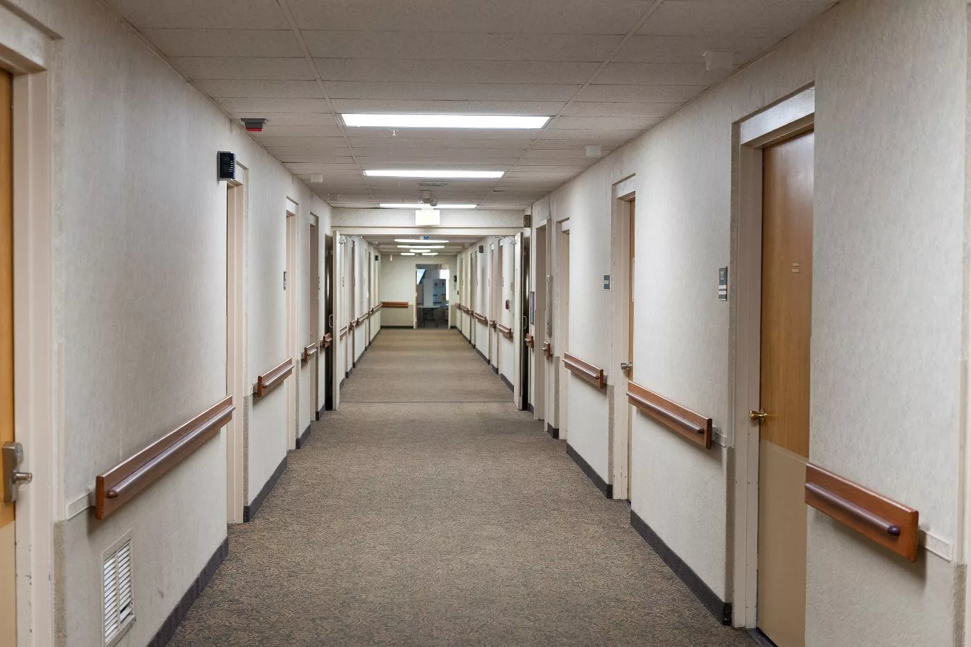 A long indoor corridor with doors on either side and bright overhead lighting.