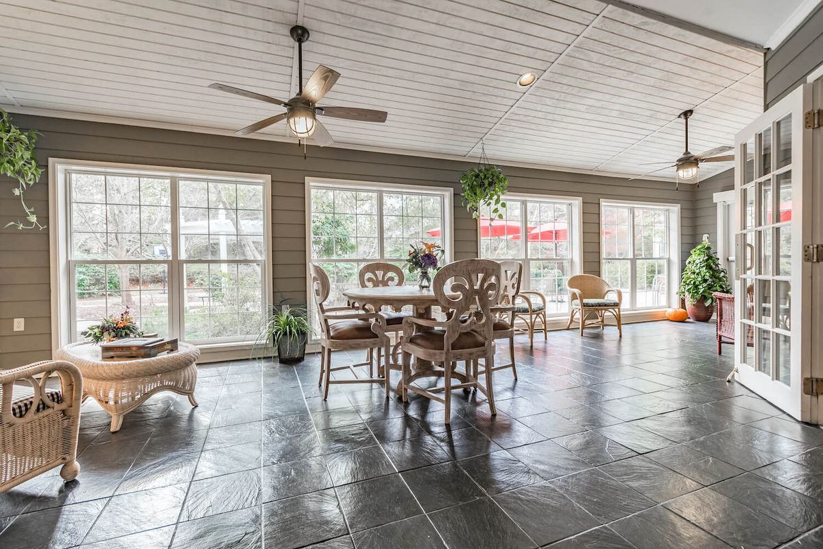 A spacious dining area with large windows, tile flooring, and a ceiling fan.