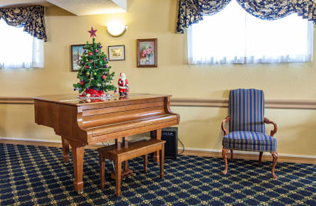 A cozy indoor setting featuring a grand piano adorned with holiday decorations, including a Christmas tree and Santa figurine.