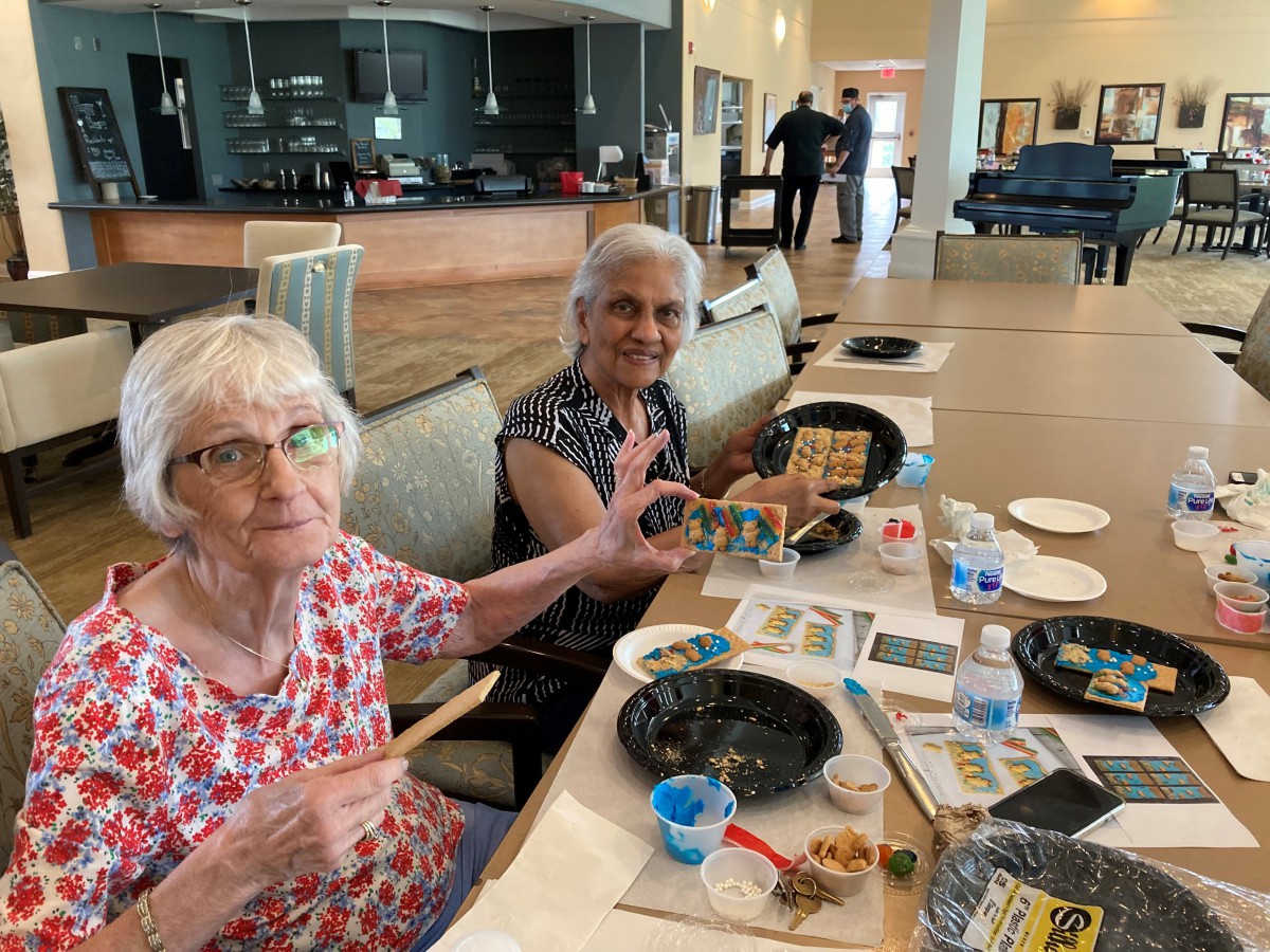 Two elderly women engage in a painting activity at a community center.