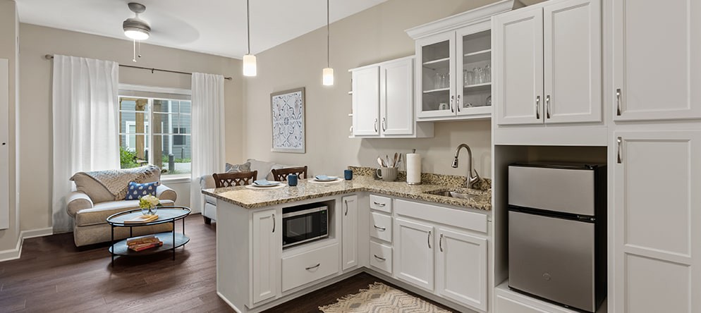 A modern kitchen with white cabinets and granite countertops, featuring pendant lighting and stainless steel appliances.