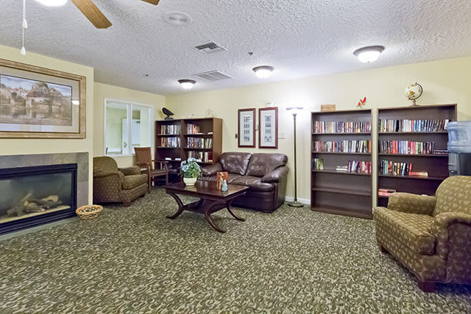 A cozy living room with bookshelves, a sofa, chairs, and a coffee table on a patterned carpet.