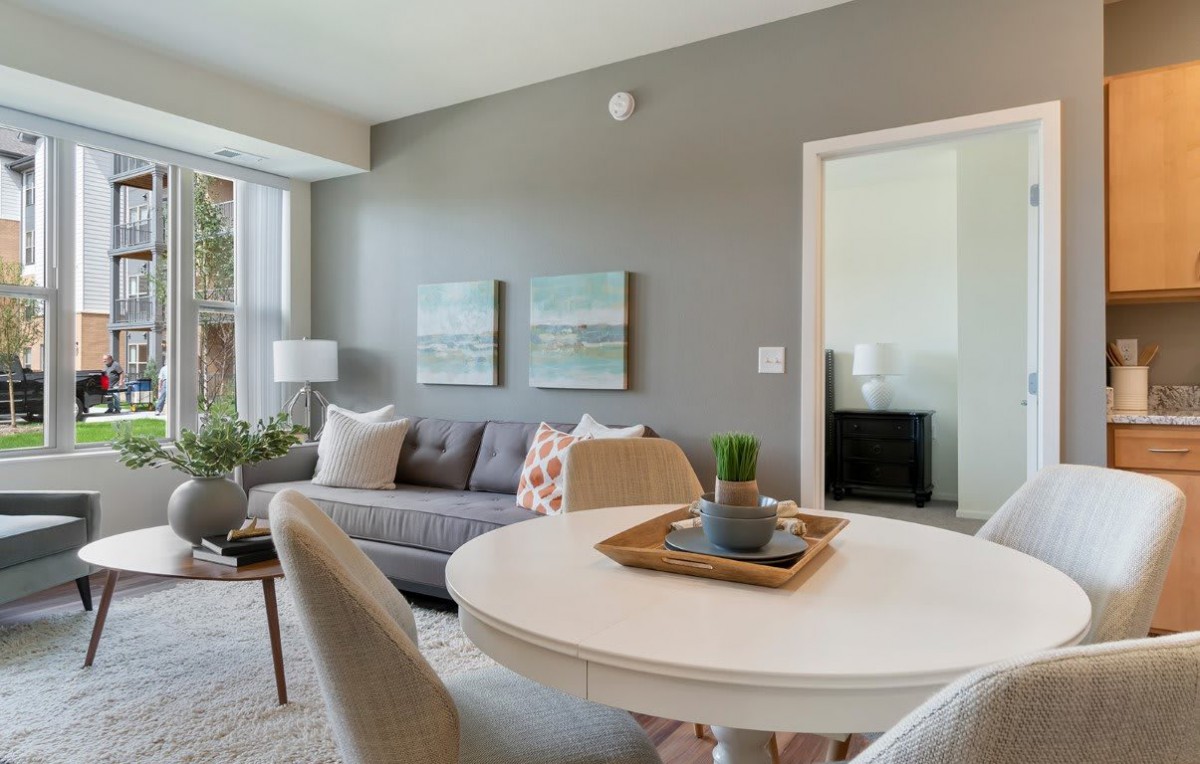 A modern living room with stylish decor, featuring a comfortable sofa, dining table, wall art, and ample natural light.