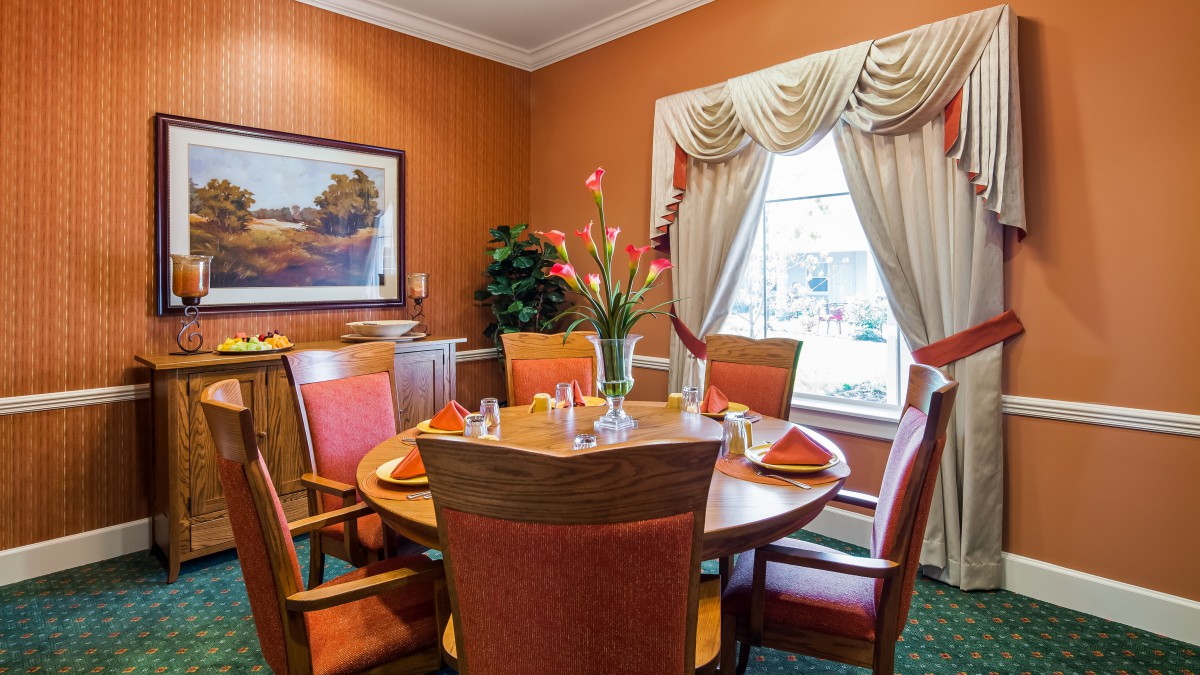 A cozy dining room with a round table set for four, featuring elegant window curtains and floral centerpiece.
