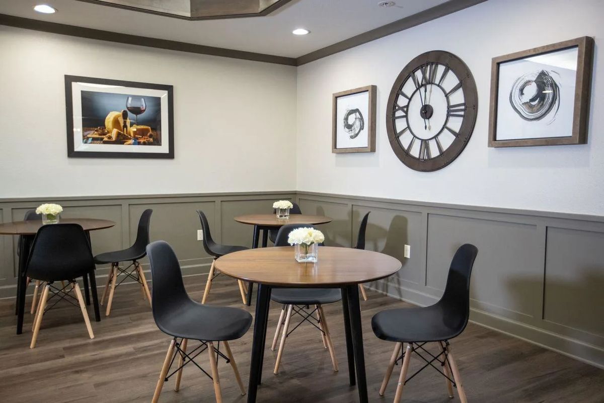 A modern cafe interior featuring round tables, black chairs, wall art, and a large decorative clock.