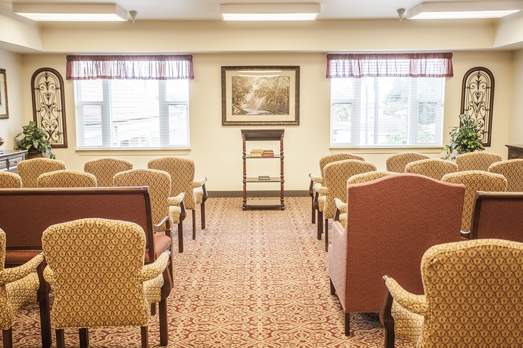 An empty lecture room with rows of chairs, a podium, and windows letting in natural light.