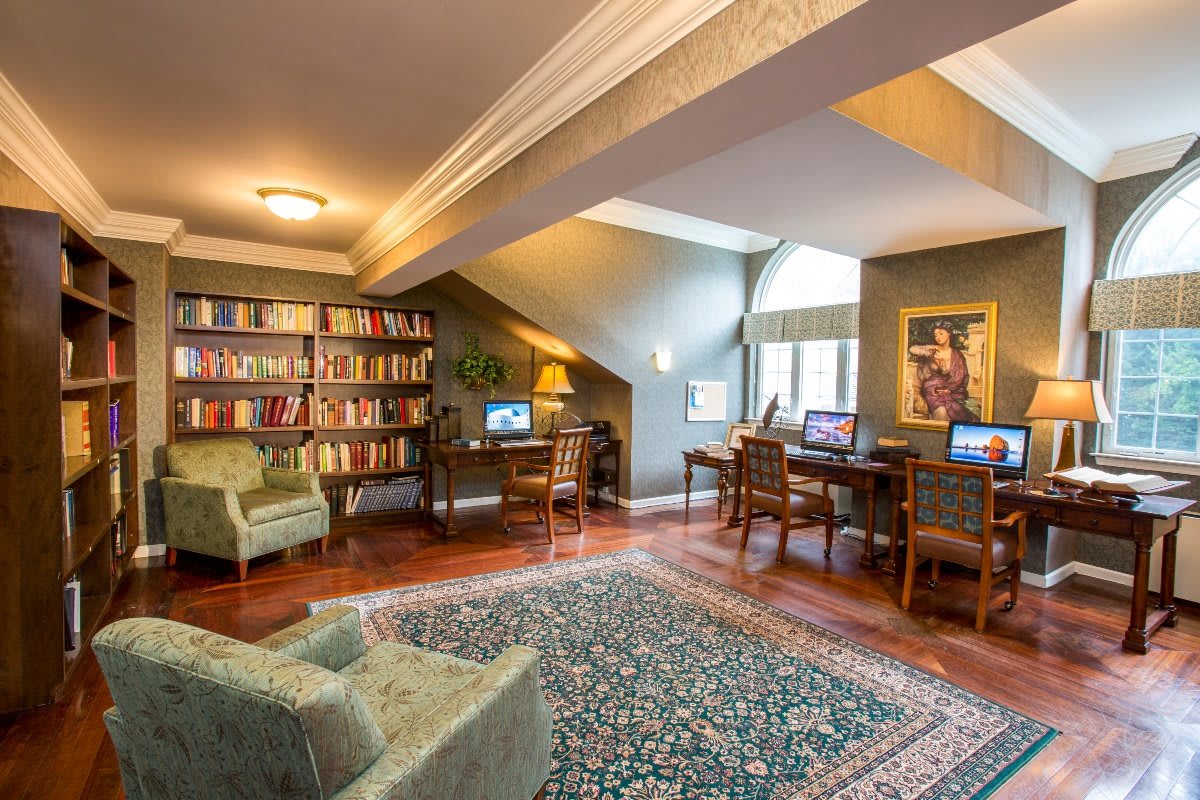 A cozy library room with bookshelves, computers, and comfortable seating.
