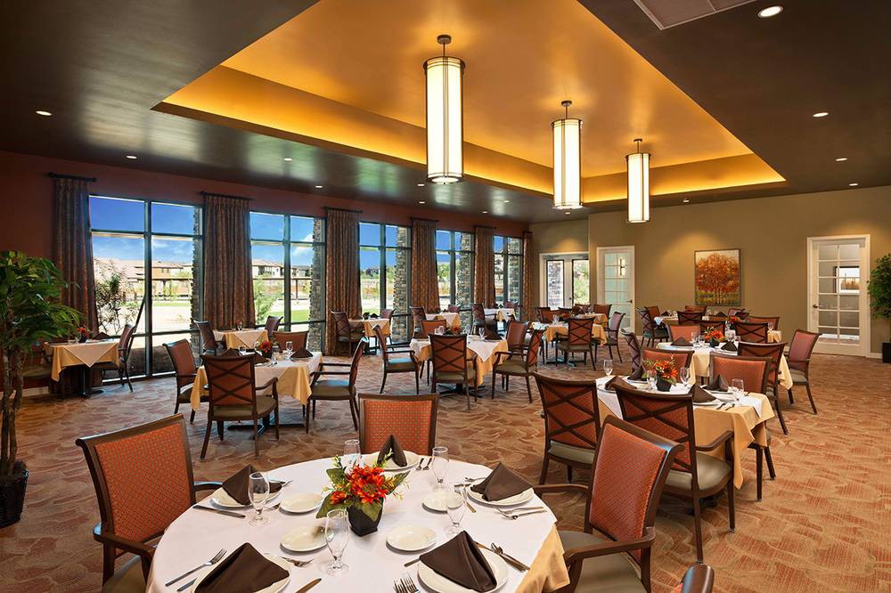 An elegant dining room with neatly arranged tables and chairs, featuring large windows and warm lighting.