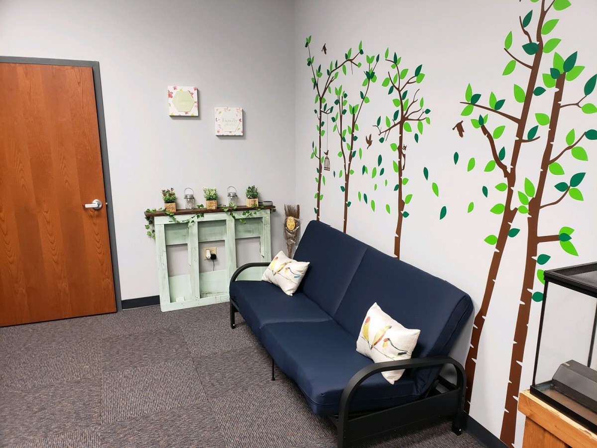 A cozy waiting room with a blue couch and tree-themed wall art.