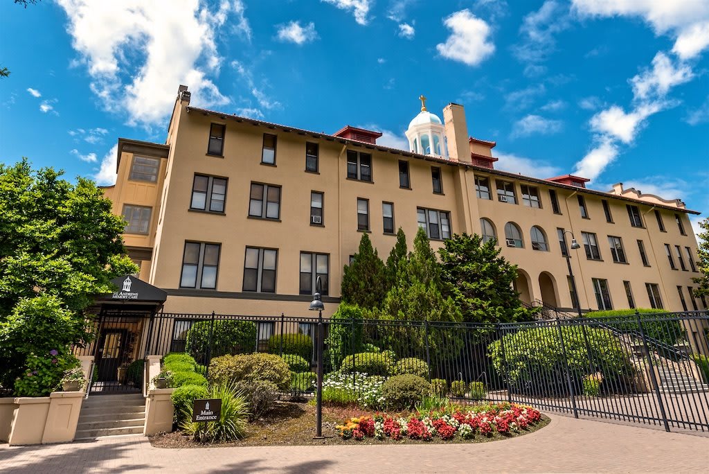 A beautiful hotel building surrounded by well-maintained gardens under a partly cloudy sky.