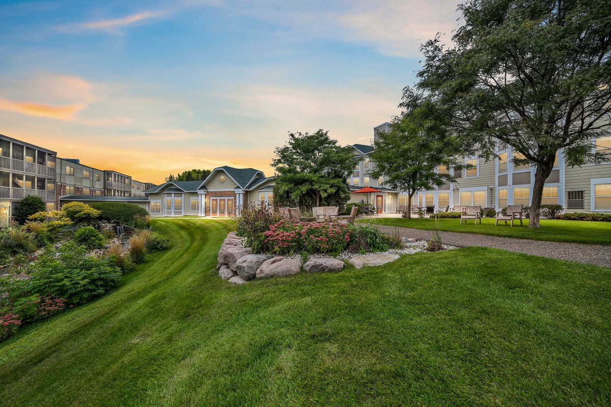 A serene suburban neighborhood with well-maintained gardens and houses under a colorful sunset sky.