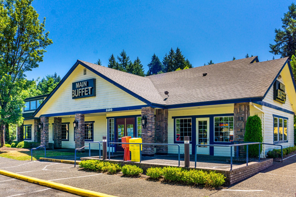 A restaurant with a buffet sign, featuring a spacious parking lot and clear blue skies.